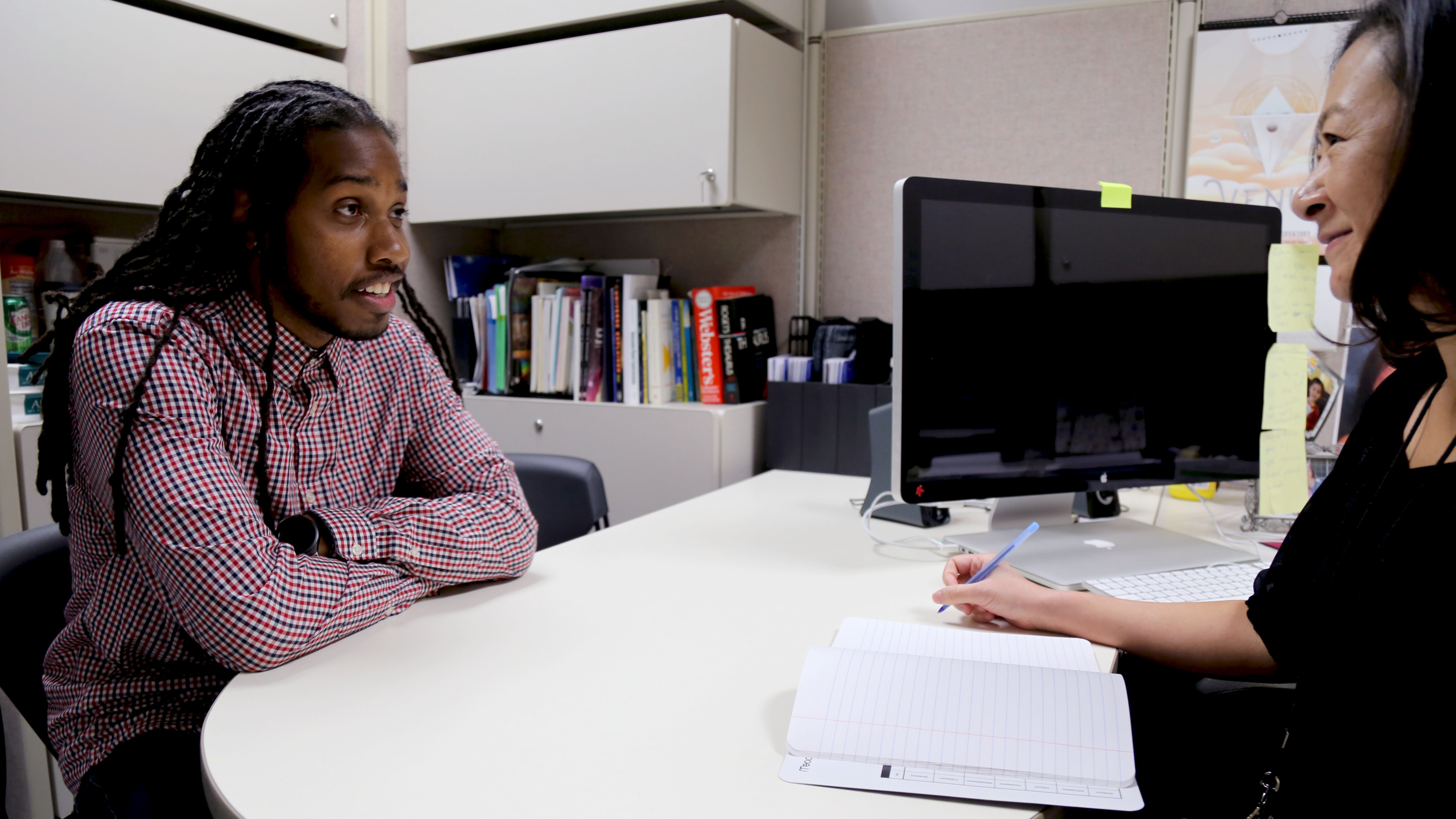 A new employee sits across from a program coordinator in an office setting.