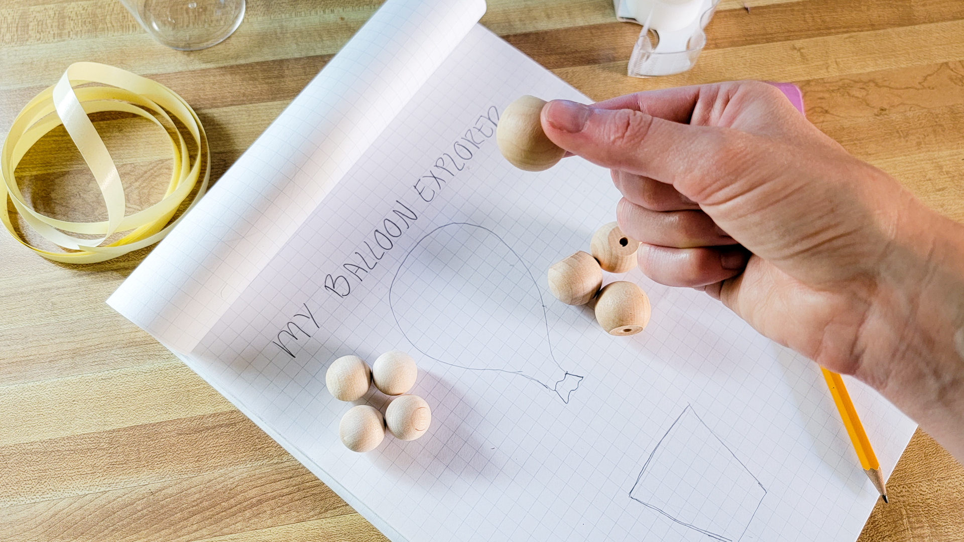A pile of small wooden beads is shown next to a pile of larger wooden beads. A person holds one of the beads as if to decide whether or not to use it.