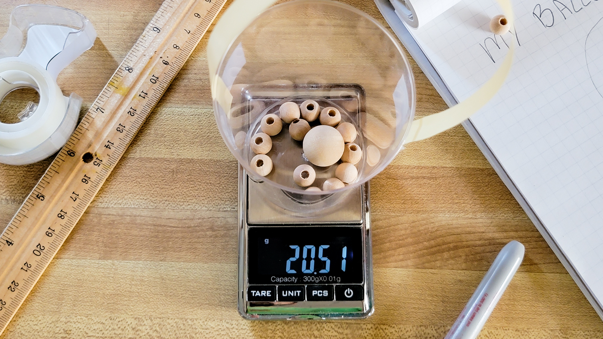 The gondola, with the ribbon and tape still attached and the wooden beads inside, sits on a small digital scale.