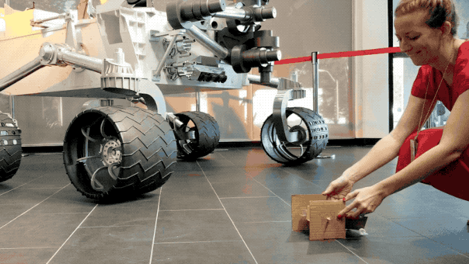 A woman releases a cardboard rover and its wheels spin as it hops forward.