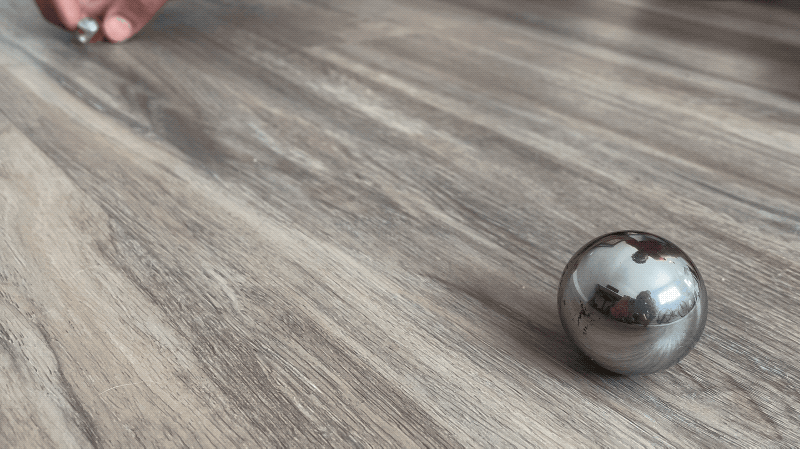 A small marble is rolled toward a large metal sphere. The marble bounces off the metal sphere and rolls back in the other direction while the metal sphere wobbles slightly.