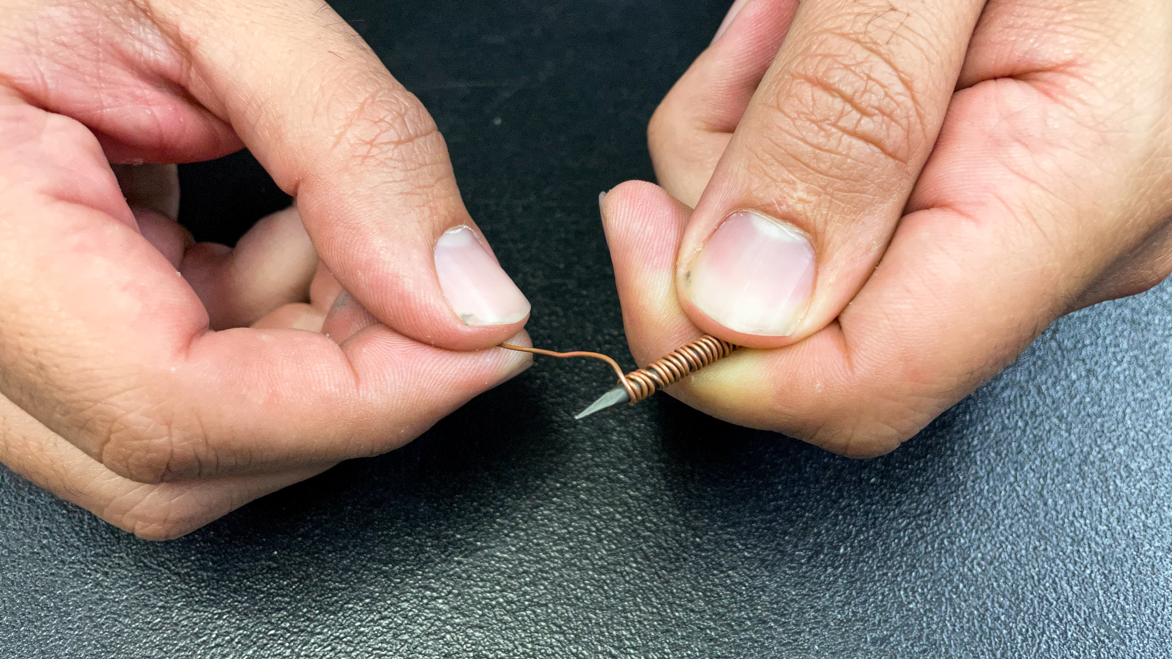 A person wraps a piece of wire tightly around a small nail.