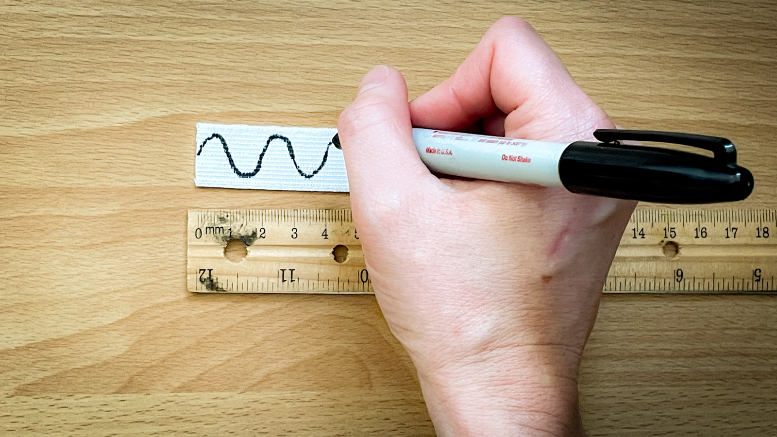 A person draws a wavy line connecting the dots drawn on a piece of elastic.