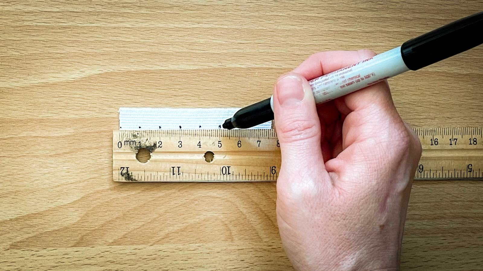 A person uses a ruler to draws evenly spaced dots on a strip of elastic.