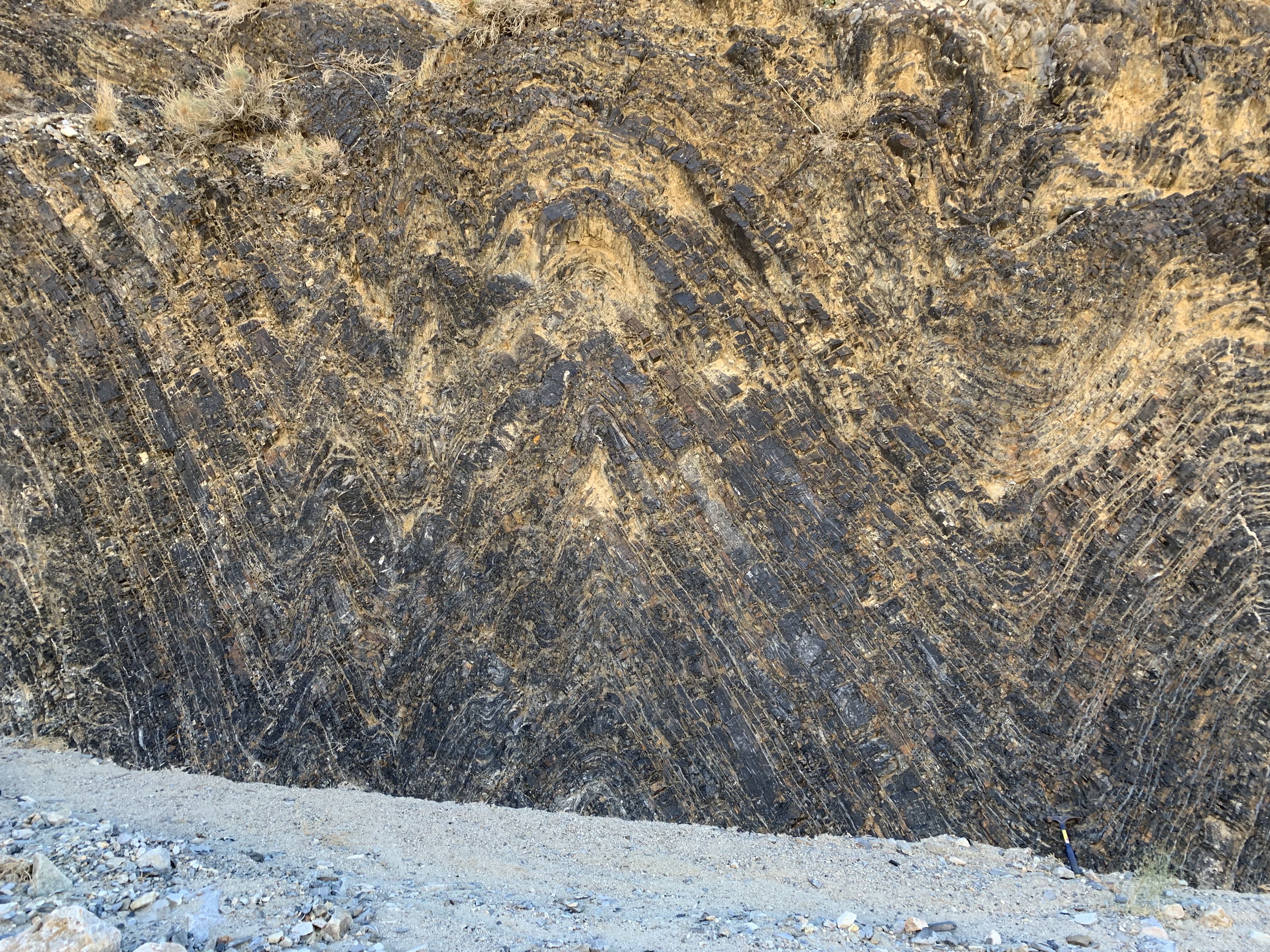 Layers of rock form a pattern of upward facing arrows on a rock wall.