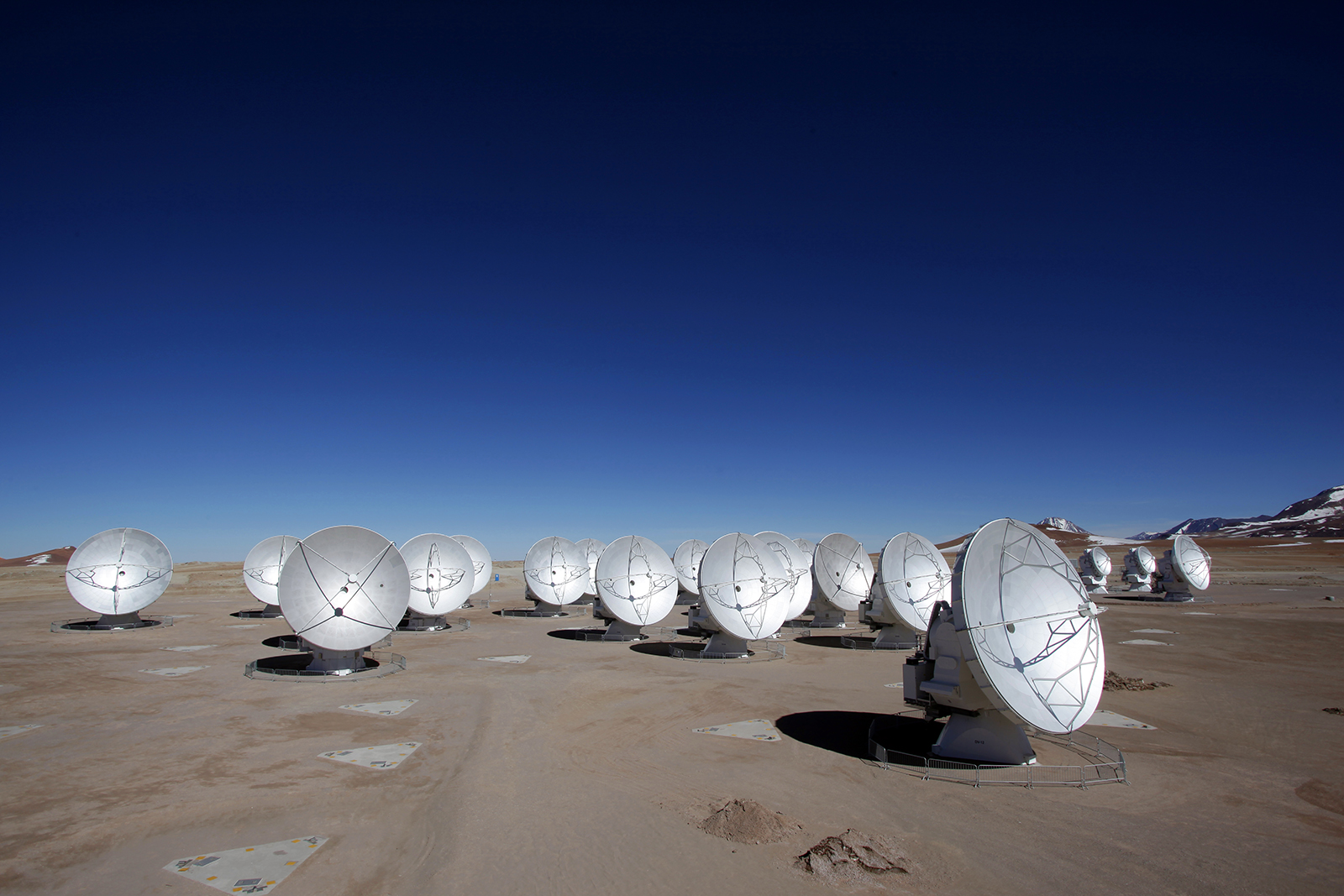 More than a dozen forward-facing antennas are installed on barren land surrounded by red and blue-violet mountains in the distance.