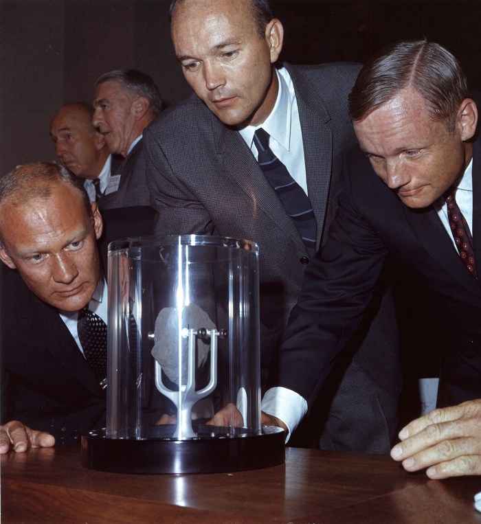 The Apollo 11 astronauts crowd around a lunar sample contained in a protective case.