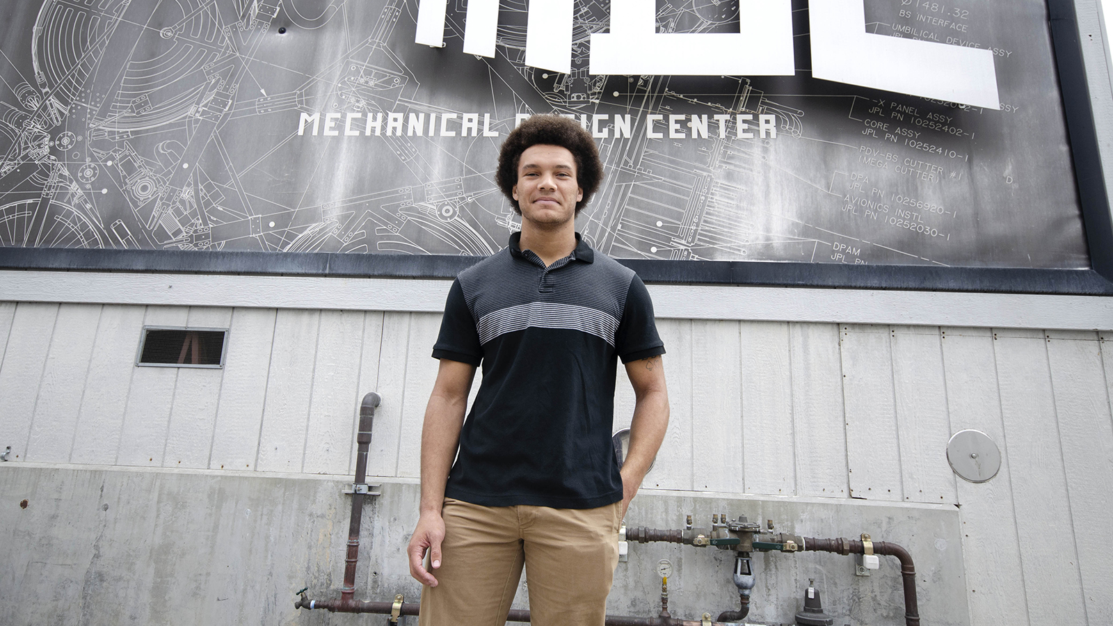 Brandon Ethridge stands in front of a mural made to look like a blueprint on the Mechanical Design Building at JPL.