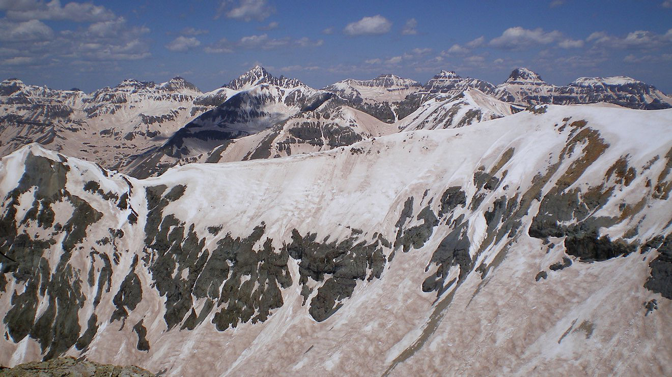 Sharp mountain peaks are covered in splotches of snow with a fine coating of dust visible on top of the snow.