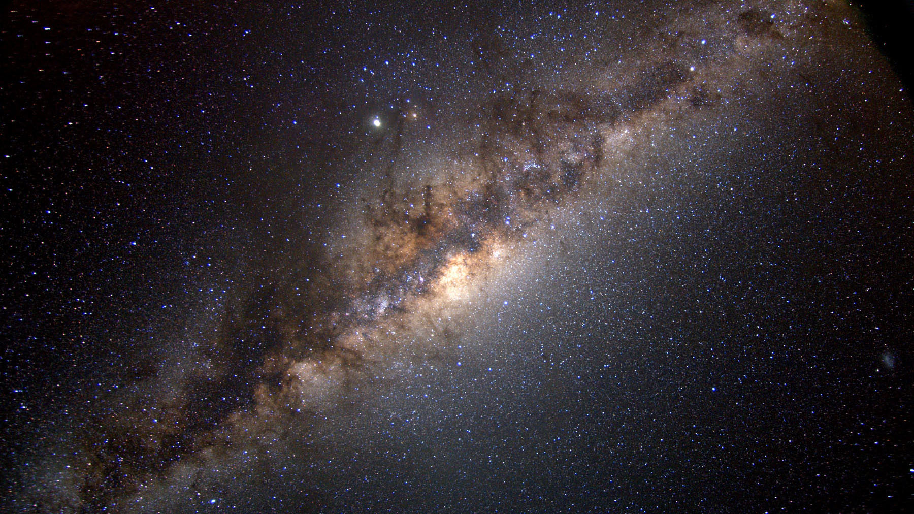 A speckled field of bluish stars is intersected by a diagonal strip of purple and brown clouds covering a glowing yellow band beyond.