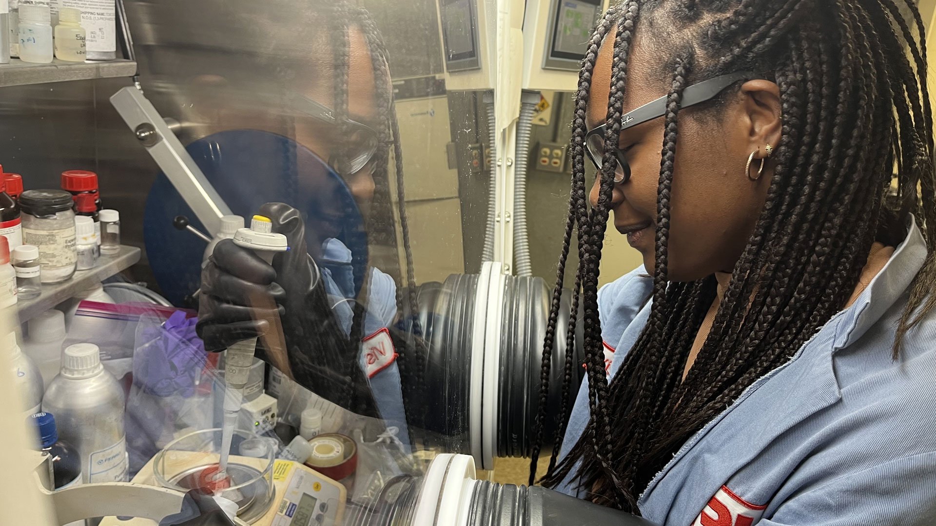 Robinson's long braids fall around her face and glasses as she operates a large dropper with her hands and arms inside the glove box.