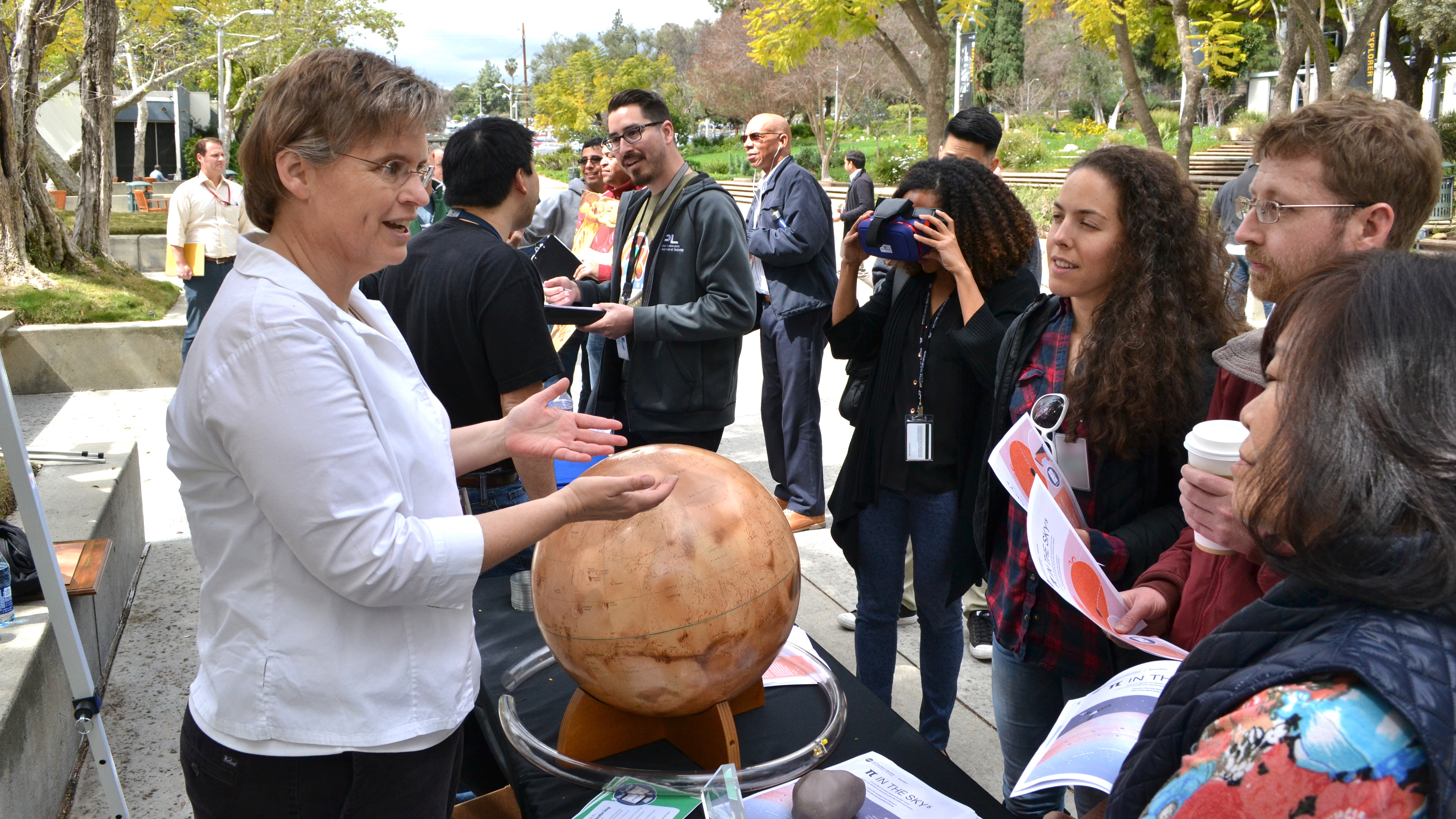 Ota Lutz stands behind a tabletop Mars globe and speaks with a group of people