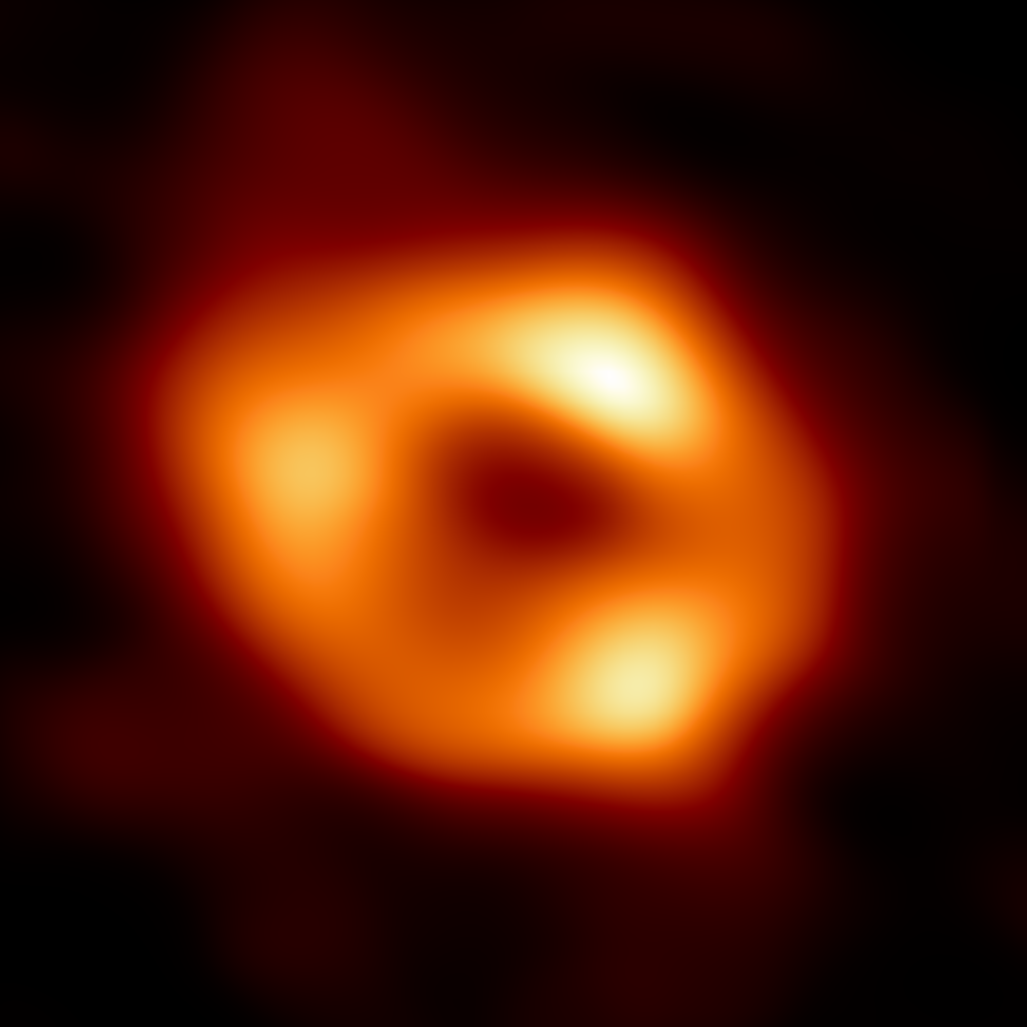 A slightly oblong donut-shaped ring of glowing warm dust especially bright at spots on the top, left, and right surrounds a black hole.