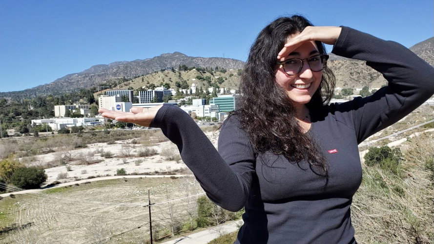 Shirin Nataneli holds out her hand, showcasing the JPL campus in the background.