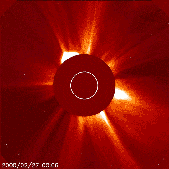 A solid red circle with a smaller white-outlined circle inside it is centered over the disk of the Sun. Streams of yellow, red, and orange shoot out from the Sun, all around the solid circle, while a large solar flare bursts out of the upper left portion of the circle. A time stamp in the corner reads 2000/02/27.
